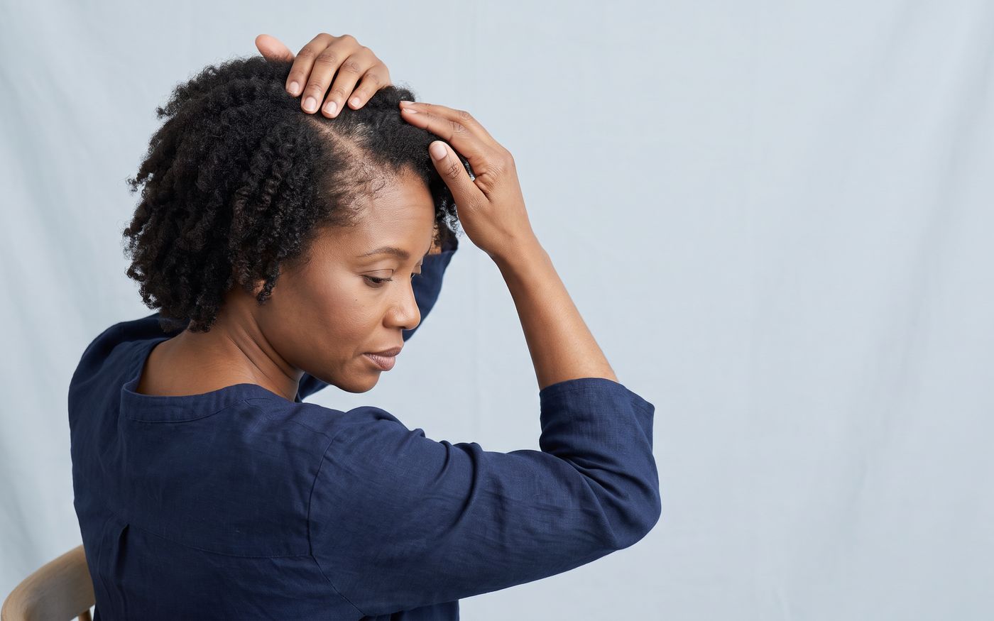 Woman gently parting natural hair to show central thinning in female hair loss