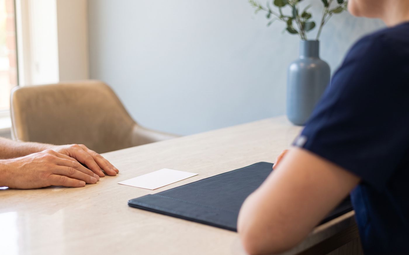 Patient hands near blank card and navy folder for eyebrow transplant payment planning