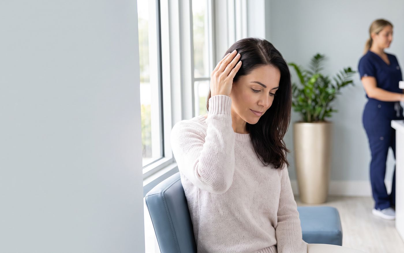 Woman parting hair beside clinic window during female hair transplant consultation